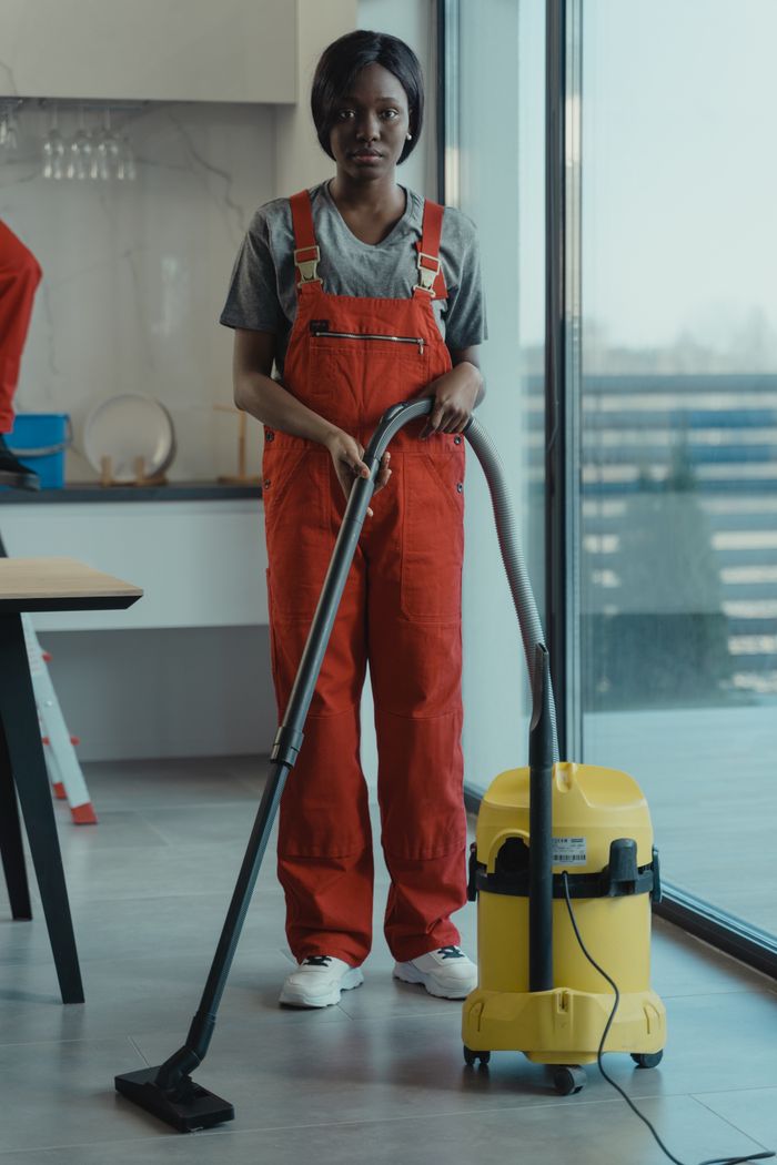 why-choose-us An adult woman in red coveralls operates a vacuum cleaner in a modern indoor setting, focusing on cleaning tasks.