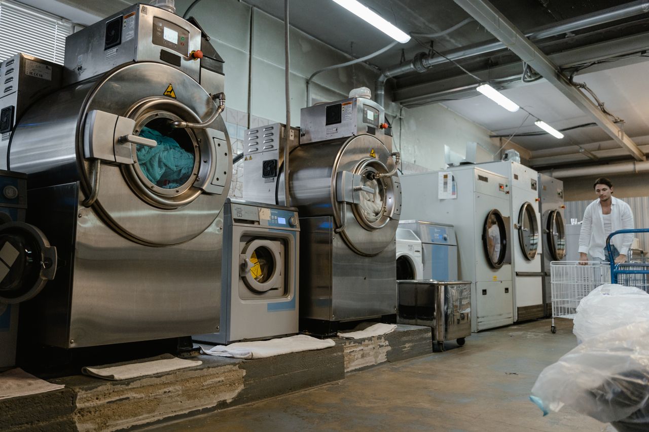 services-01 Industrial laundromat interior with large washing machines and a man pushing a trolley.