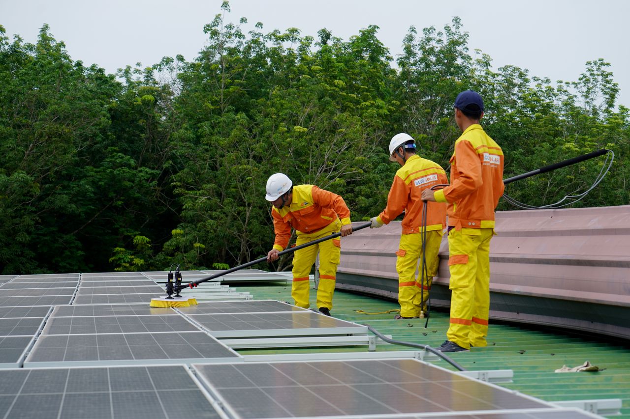 services-02 Three technicians in uniforms and hardhats clean rooftop solar panels in a renewable energy project.